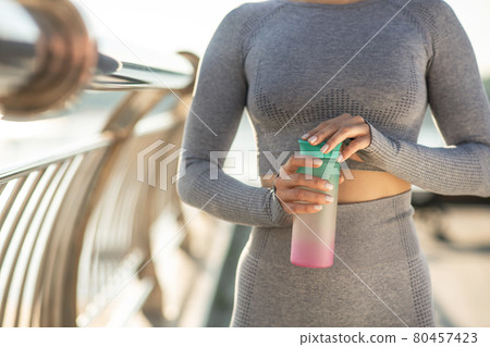 Young girl in grey sportswear with a bottle of water in hands 80457423