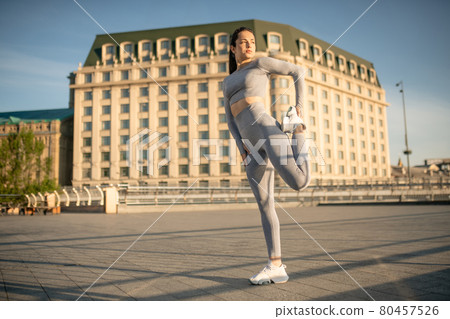 Young female sportsperson stretching her legs and looking concentrated 80457526