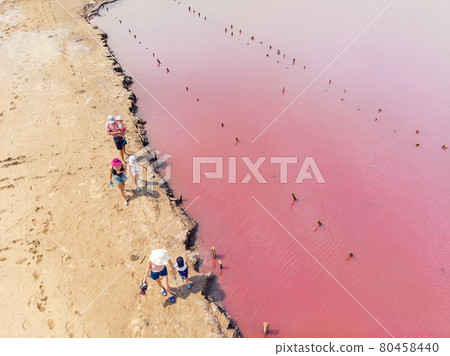Aerial drone view tourist family group people walking along water edge shore coast of bright colorful pink salt lake on hot sunny summer day. Unusual travel destination and tourism concept 80458440