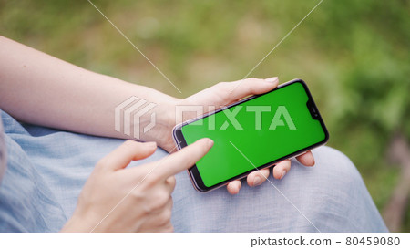 Beautiful girl holding in her hands a smartphone with a green screen. Beautiful girl holding in her hands a smartphone with a green screen. 80459080