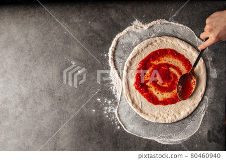 Making a pizza spreding tomato sauce on the dough Making a pizza spreding tomato sauce on the dough 80460940