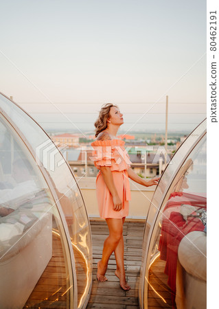 beautiful woman in a pink dress in a rooftop cafe at sunset beautiful woman in a pink dress in a rooftop cafe at sunset 80462191