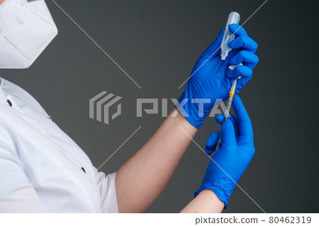 Close-up studio shot of unrecognizable nurse in blue gloves holding and filling up vaccine to syringe on black isolated background. 80462319