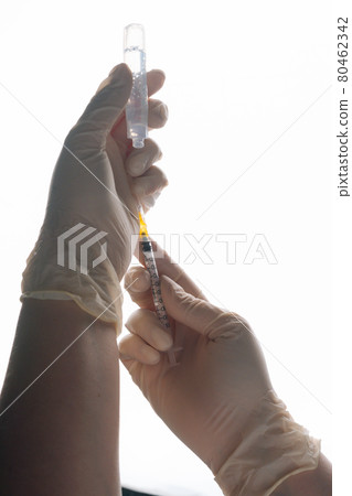 Vertical close-up studio shot of unrecognizable doctor in white gloves filling vaccine to syringe on white isolated background. Vertical close-up studio shot of unrecognizable doctor in white gloves filling vaccine to syringe on white isolated background. 80462342
