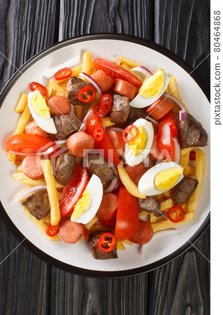 Pique macho is a very popular dish from Bolivia made of beef cuts and fried sausages with fries, eggs, chili peppers and tomatoes closeup in the plate. Vertical top view 80464868