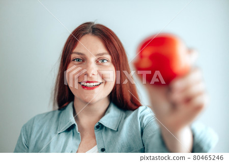 Portrait of a cheerful young woman eating red apple on gray wall background. Healthy nutrition diet. Apple vitamin snack. Portrait of a cheerful young woman eating red apple on gray wall background. Healthy nutrition diet. Apple vitamin snack. 80465246