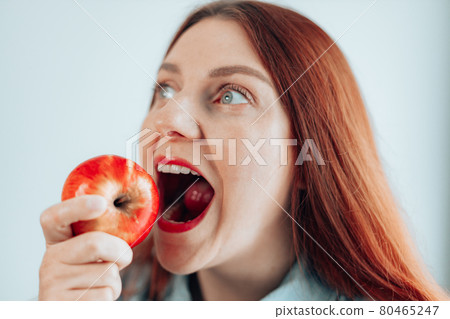 Portrait of a cheerful young woman eating red apple on gray wall background. Healthy nutrition diet. Apple vitamin snack. Portrait of a cheerful young woman eating red apple on gray wall background. Healthy nutrition diet. Apple vitamin snack. 80465247