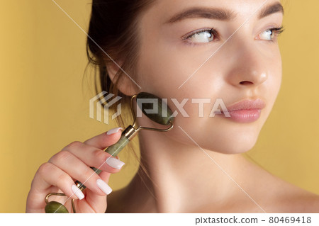 Close up portrait of young female fashion model isolated on yellow studio background. Beautiful caucasian woman making face massage. Close up portrait of young female fashion model isolated on yellow studio background. Beautiful caucasian woman making face massage. 80469418