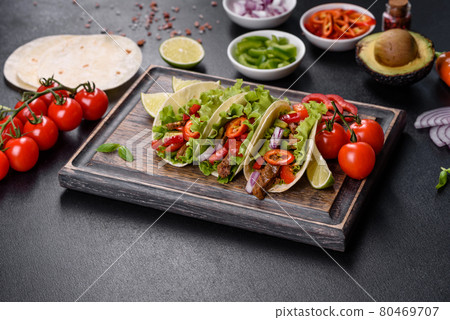Mexican tacos with beef, tomatoes, avocado, onion and salsa sauce on a dark concrete background Mexican tacos with beef, tomatoes, avocado, onion and salsa sauce on a dark concrete background 80469707