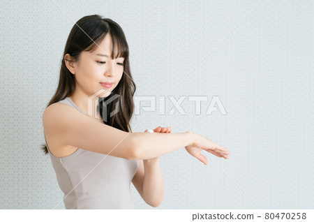 Young woman applying moisturizing cream to her arms 80470258