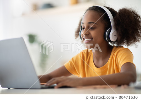 Cheerful black girl studying online, using laptop and headset Cheerful black girl studying online, using laptop and headset 80471630