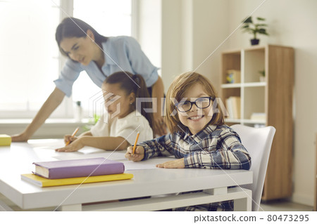 Portrait of cute little elementary student in glasses sitting at his desk in classroom Portrait of cute little elementary student in glasses sitting at his desk in classroom 80473295