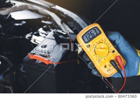 Mechanic checking car battery voltage with digital multimeter 80473360
