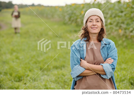 Mature cheerful female farmer in beanie and workwear looking at you with smile Mature cheerful female farmer in beanie and workwear looking at you with smile 80473534