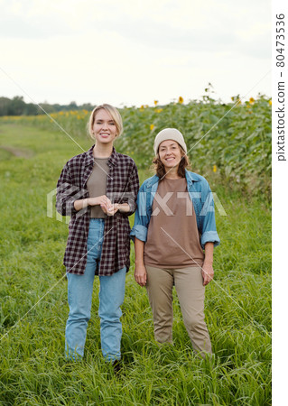 Two cheerful female farmers in workwear looking at you with smiles at farm Two cheerful female farmers in workwear looking at you with smiles at farm 80473536