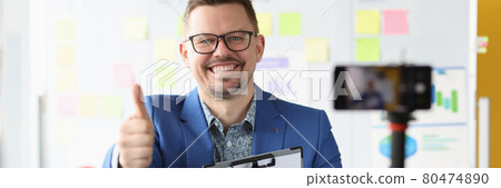 Smiling businessman holds thumbs up and records business training on video Smiling businessman holds thumbs up and records business training on video 80474890