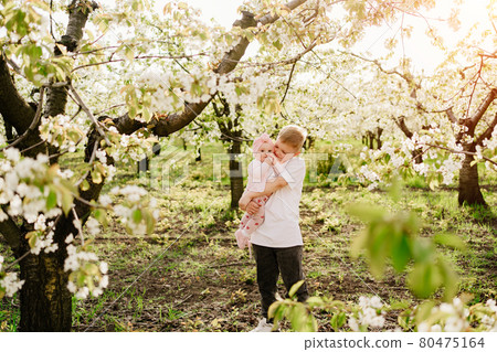 brother holds sister in spring flower garden. girl after surgery on harelip brother holds sister in spring flower garden. girl after surgery on harelip 80475164