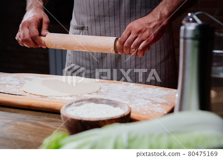 hands roll the dough into a thin layer. Cooking pizza, noodles or pitta at home hands roll the dough into a thin layer. Cooking pizza, noodles or pitta at home 80475169