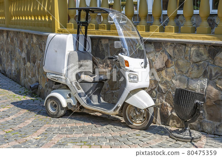 White compact 3-wheel scooter against a stone wall White compact 3-wheel scooter against a stone wall 80475359