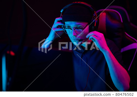 Close-up of the face of a professional video game player at an esports tournament. A cyberathlete wearing headphones and a headset. 80476502