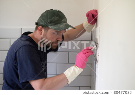 Worker applies grey grout at white tiles with rubber trowel. Worker applies grey grout at white tiles with rubber trowel. 80477083