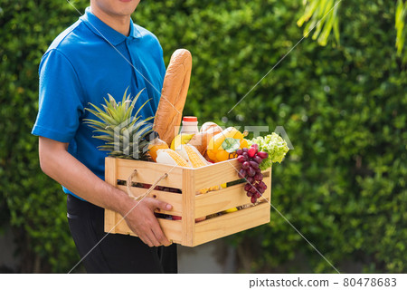 Man farmer wears delivery uniform he holding full fresh vegetables and fruits in crate wood box Man farmer wears delivery uniform he holding full fresh vegetables and fruits in crate wood box 80478683