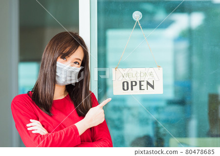 Woman wear face mask point finger she notice sign wood board label "WELCOME OPEN" hanging through glass door shop, Business turn open after coronavirus disease Woman wear face mask point finger she notice sign wood board label "WELCOME OPEN" hanging through glass door shop, Business turn open after coronavirus disease 80478685