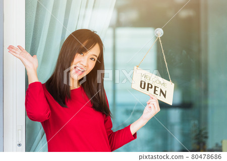 Woman glad smiling she notice sign wood board label "WELCOME OPEN" hanging through glass door front shop Woman glad smiling she notice sign wood board label "WELCOME OPEN" hanging through glass door front shop 80478686