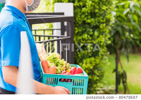 Delivery man wearing face mask protect he delivering fresh food vegetable in plastic box Delivery man wearing face mask protect he delivering fresh food vegetable in plastic box 80478687