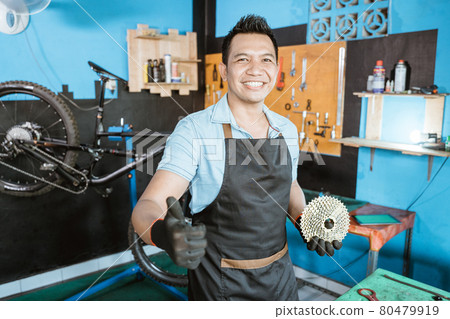 handsome bicycle mechanic in smiling apron holding freewheel with thumb handsome bicycle mechanic in smiling apron holding freewheel with thumb 80479919