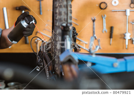 close up of a mechanic's hand wearing gloves using chain lube lubricating the chain and freewheel close up of a mechanic's hand wearing gloves using chain lube lubricating the chain and freewheel 80479921