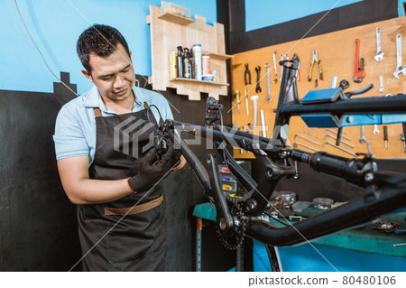 a bicycle mechanic in apron holds the rear mech as it attaches to the frame 80480106