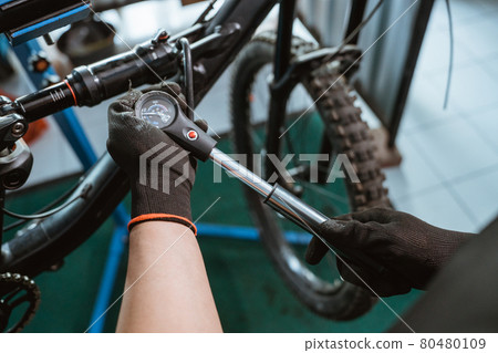 bicycle mechanic's hand in gloves using a pressure gauge pump to adjust suspension 80480109