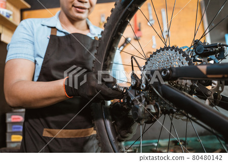 hand of a mechanic wearing gloves setting bicycle spoke 80480142