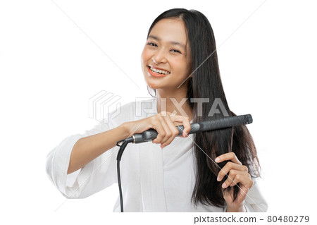 Smiling woman straightening hair with hair straightener 80480279