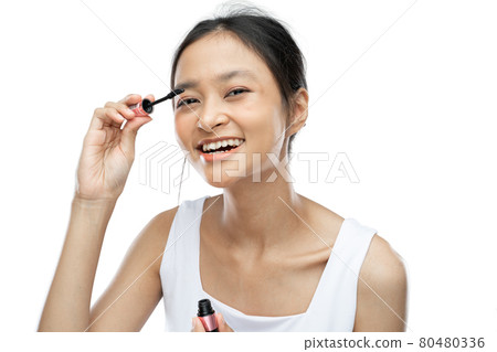 asian woman wearing white underdress using mascara to apply makeup 80480336