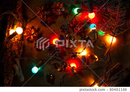 Christmas pine cones, lights and parts of tree bark. Colorful vintage stones. Bronze surface background. Selective lighting scene. Top view photo. 80481186