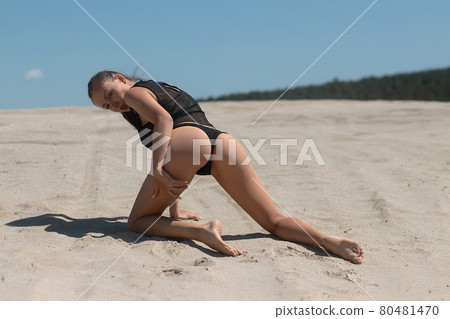 Slim woman in black underwear kneeling on sand 80481470