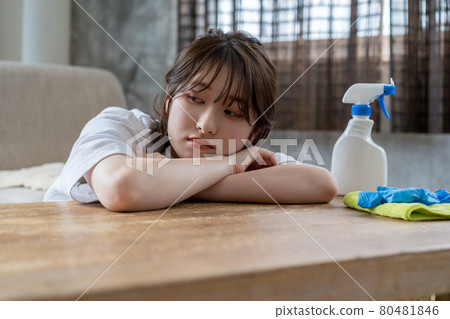 A woman who looks moody because she is tired of cleaning (housework) and lies on her stomach at the table. 80481846