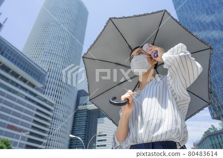A business woman walking in the business district (in front of Nagoya station) while wiping her sweat with a sunshade A business woman walking in the business district (in front of Nagoya station) while wiping her sweat with a sunshade 80483614