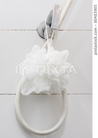 The white bath fluffy is hanging on the shower valve near the white tile wall in the bathroom. 80483905