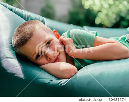 Portrait of a caucasian boy 7 years old in a green t-shirt resting on a lamzak, inflatable lounger. Portrait of a caucasian boy 7 years old in a green t-shirt resting on a lamzak, inflatable lounger. 80485274