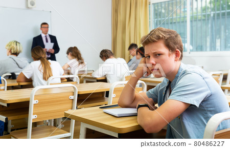 Upset teenage schoolboy sitting in classroom during lesson Upset teenage schoolboy sitting in classroom during lesson 80486227