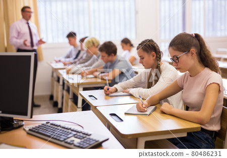 Teenagers listening to lecturer and writing in notebooks in classroom Teenagers listening to lecturer and writing in notebooks in classroom 80486231