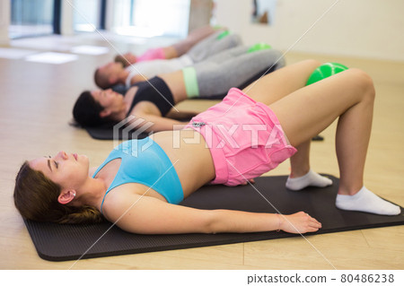 Active group of people performs an exercise with a ball clamped between the knees Active group of people performs an exercise with a ball clamped between the knees 80486238