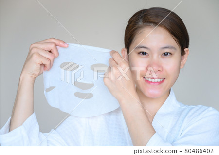 Portrait of young Asian woman holding facial mask and looking to camera. Facial mask is a creamy or thick pasted mask applied to clean or smoothen the face. 80486402