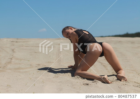 Slim woman in black underwear kneeling on sand Slim woman in black underwear kneeling on sand 80487537
