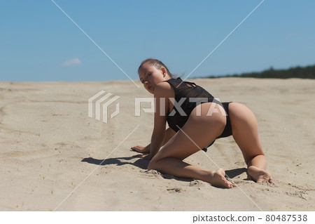 Slim woman in black underwear kneeling on sand 80487538