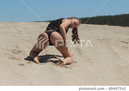 Slim woman in black underwear kneeling on sand 80487542