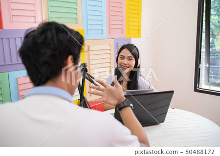 a girl wearing a headphones and chats with a guy in front of a microphone during a podcast a girl wearing a headphones and chats with a guy in front of a microphone during a podcast 80488172